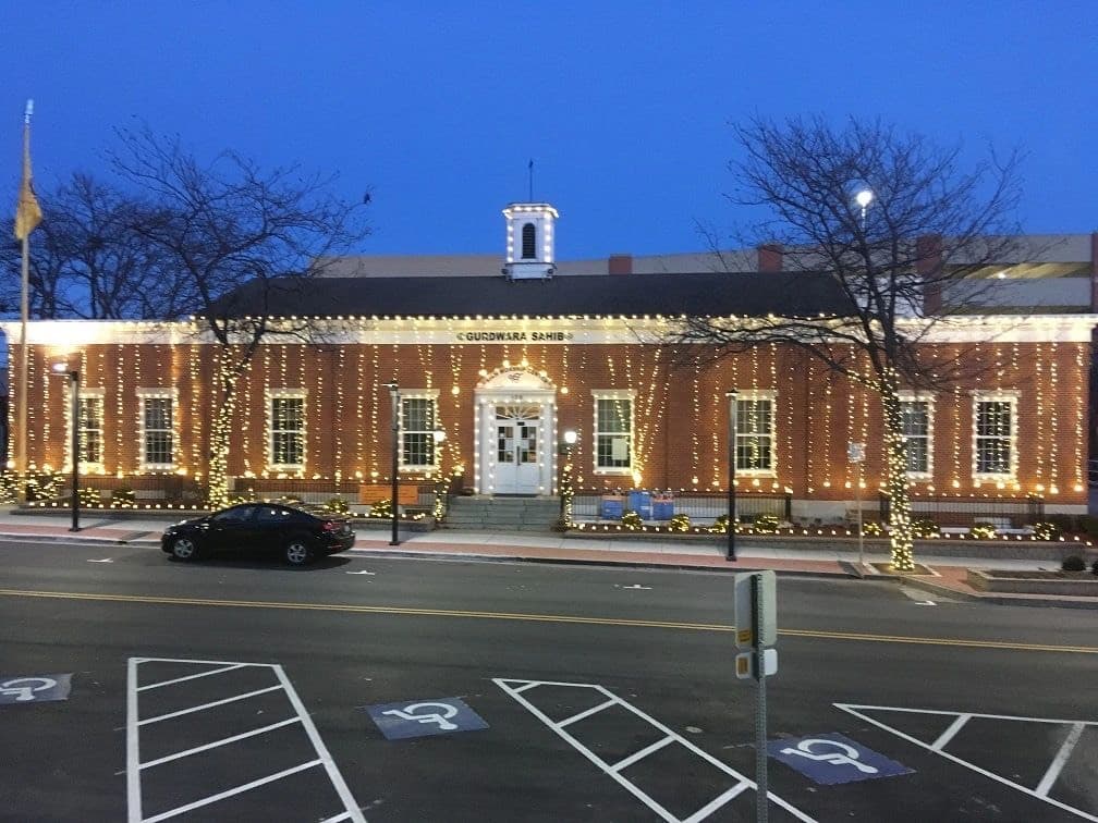 Gurdwara Nanak Darbar Sahib, the red-brick gurdwara on South Cherry Street in Olathe, strung with lights at dusk with the Nishan Sahib flying at left