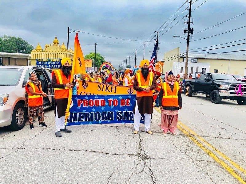 Sangat in orange safety vests carrying the 'Sikh — proud to be American Sikhs' banner and the Nishan Sahib in the Old Settlers parade, the Golden Temple float behind