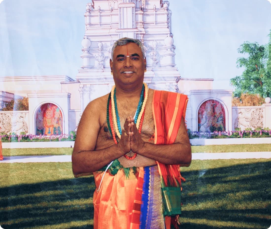 Chief Priest Shree Srinivasacharyulu Mahendrada of HTCC Kansas City in namaskar, in front of a painted backdrop of the temple gopuram