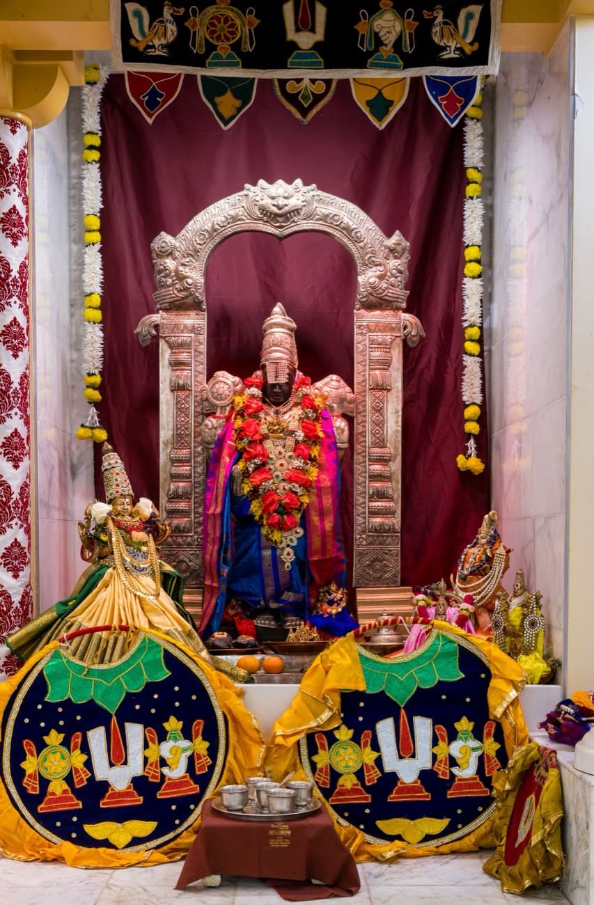 Sri Venkateswara shrine at HTCC Kansas City, the deity garlanded in red and pink with Sridevi and Bhudevi and Vaishnava namam emblems in front