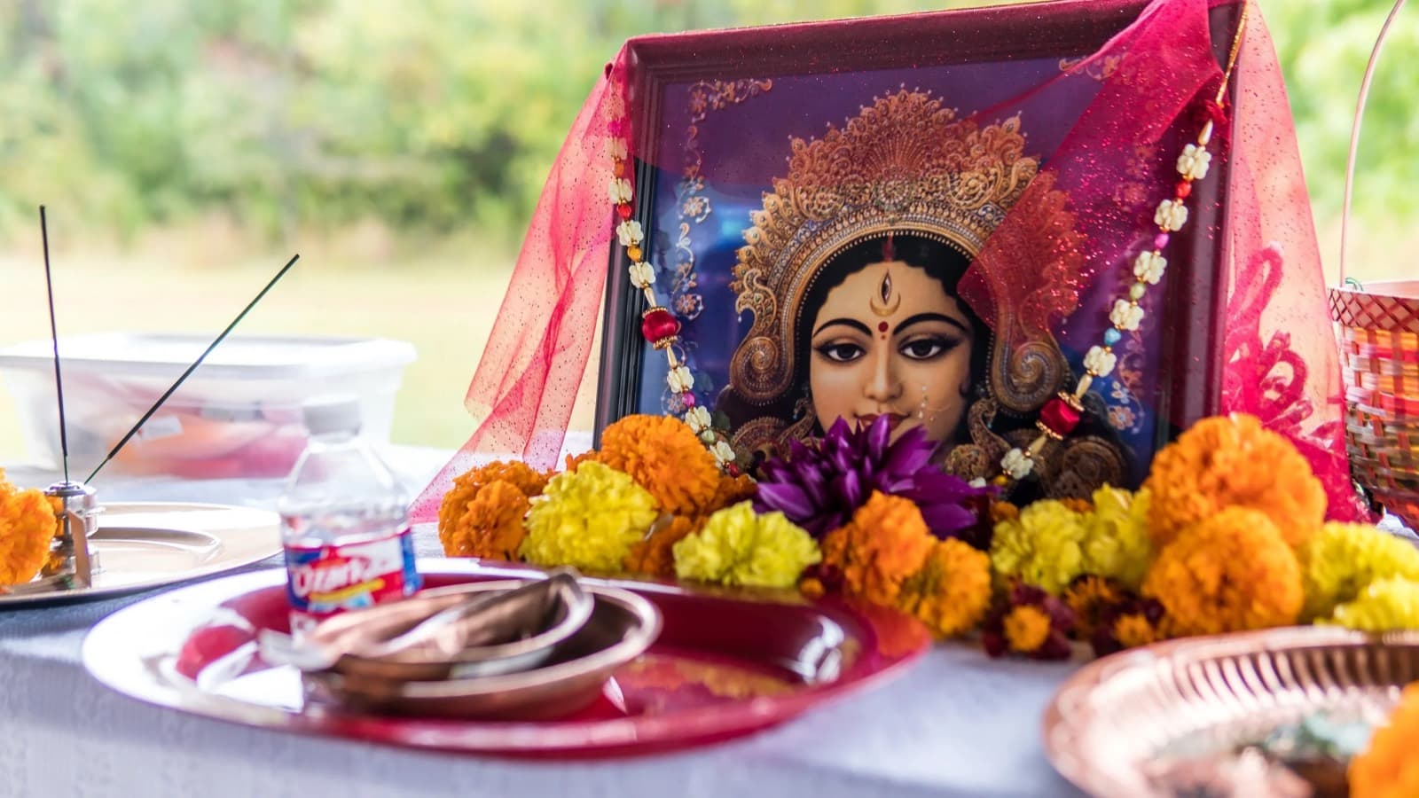 A framed image of Ma Durga draped in red, with marigolds, a copper thali and incense on a picnic table at Heritage Park for KCBA's Mahalaya morning