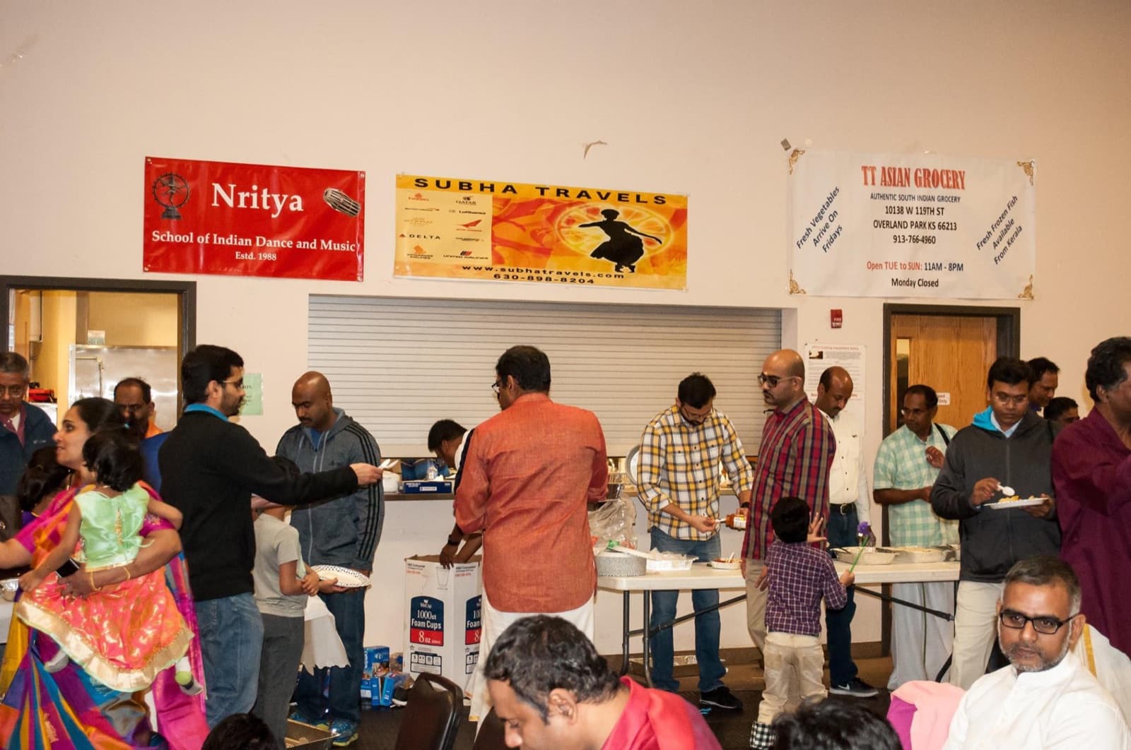 Families at the food line during KCTS Pongal 2019, sponsor banners on the wall behind